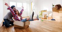 Woman sitting in a moving box with her boyfriend pushing her around their new house