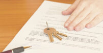 Hand holding down a paper with a set of keys and pen sitting on top