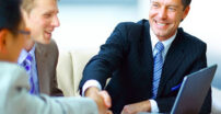 Two men shaking hands in a meeting with three men