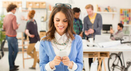 Woman smiling looking down at her phone, people are chatting in the background