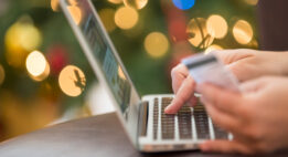 Person typing in their credit card number into a laptop with Christmas decorations in the background