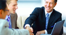 Two men shaking hands in a meeting with three men