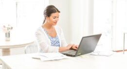 Young woman working on her computer at a table surrounded by papers