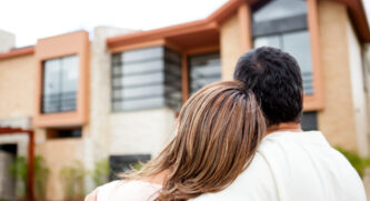 Woman leaning her head on the man's shoulders looking at a home