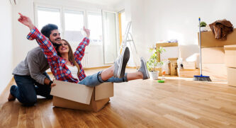 Woman sitting in a moving box with her boyfriend pushing her around their new house