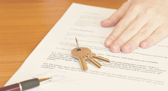 Hand holding down a paper with a set of keys and pen sitting on top