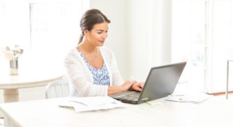 Young woman working on her computer at a table surrounded by papers